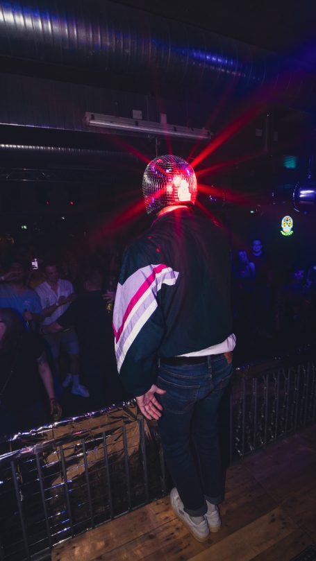 Person mit einer leuchtenden Mütze steht an einer Bar in einem Nachtclub.